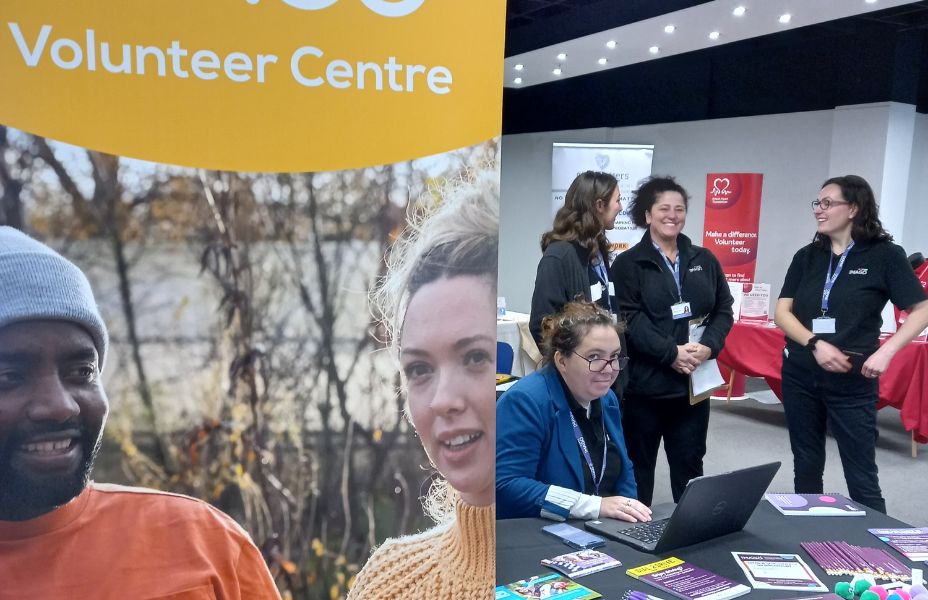 Louise from Imago Volunteer Centre sitting at a disk next to a display banner welcoming people to the volunteer fair